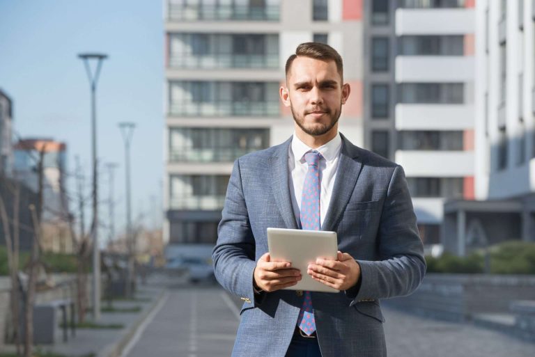 Businessman or real estate agent with tablet computer against new building